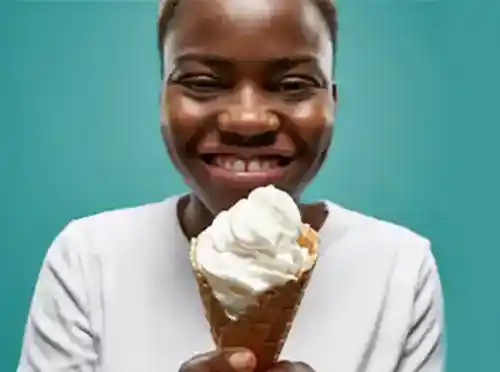 Young African-American woman smiling while holding an ice cream cone in front of her.
