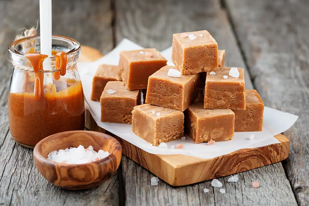 Stacked cubes of salted caramels displayed with caramel in a jar and small container of course salt.