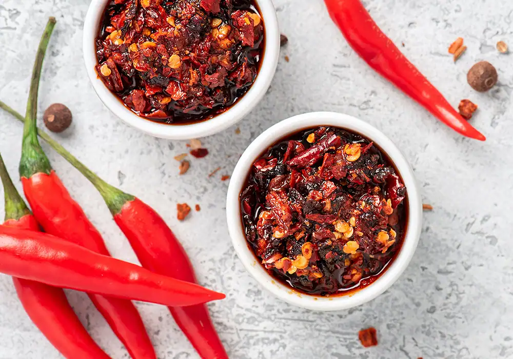 Overhead view of fresh chili peppers and chili pepper oils in bowls.