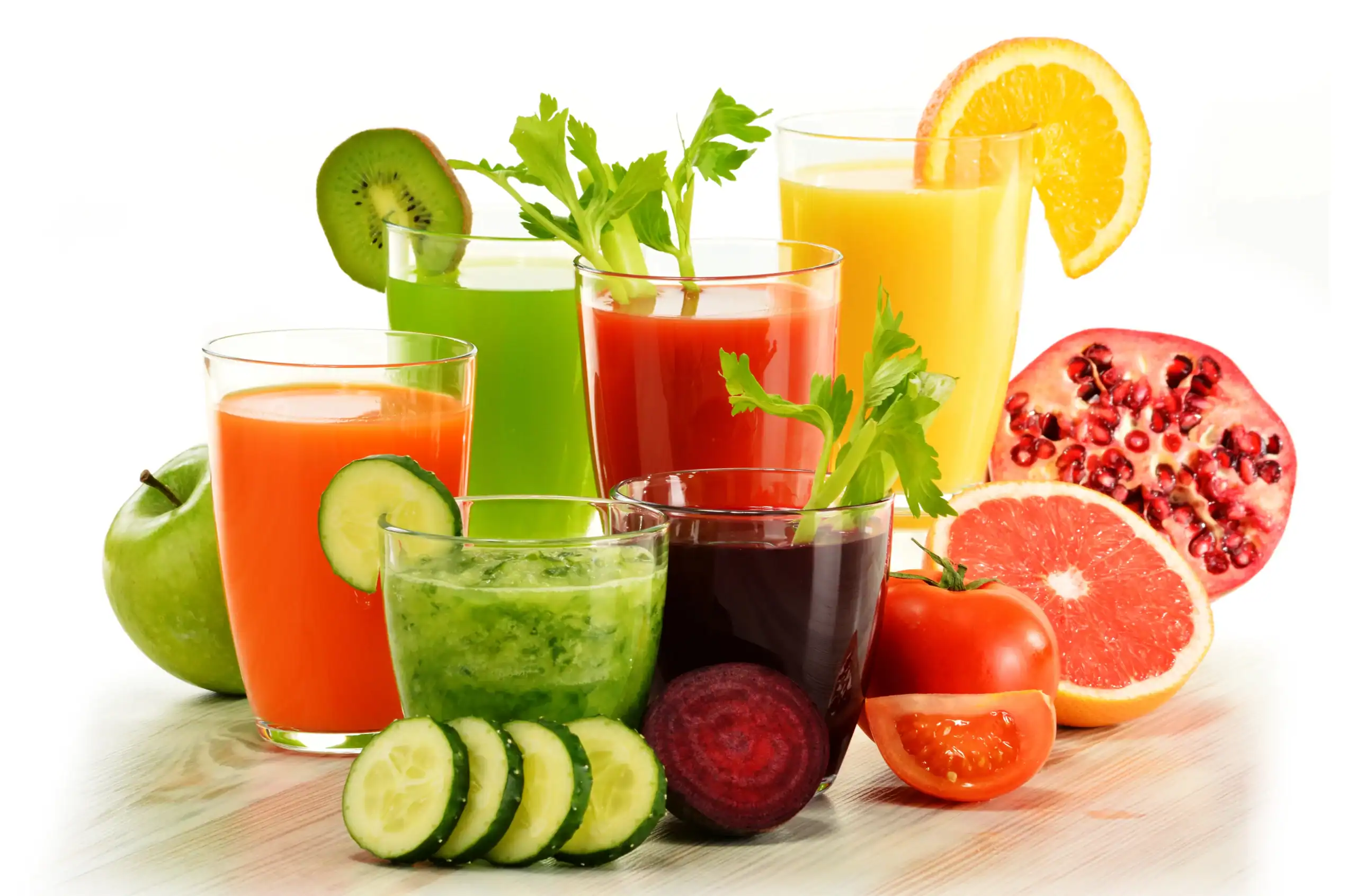 Array of glasses filled with fruit and vegetable juices surrounded by cut fruits